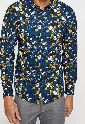 Chemise à manches longues à boutons en bleu nuit avec un motif floral multicolore, présentant des accents jaunes, blancs et noirs ; texture de tissu lisse.