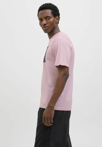 Lyserød t-shirt med kort ærme og et grafisk print på brystet. Blødt bomuldsstof med en afslappet pasform, stylet med sorte bukser.