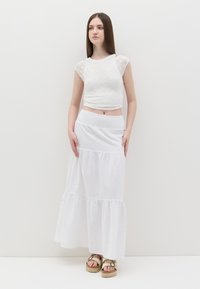 Top in cotone bianco con motivo testurizzato e maniche corte, abbinato a una gonna bianca lunga fino al pavimento a strati. Gli espadrillas completano l'outfit.