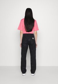 Pink cropped t-shirt and black camo cargo pants, featuring pockets and a tag on the back, paired with white sneakers. Long dark hair visible.