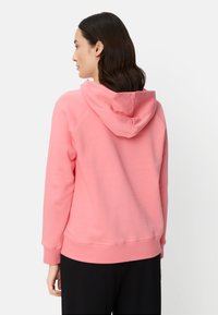 Pink cotton hoodie with a drawstring hood, ribbed cuffs, and hem. Smooth texture, relaxed fit, and raglan sleeve design.