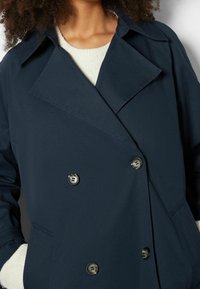 Giacca doppiopetto blu navy realizzata in tessuto liscio con ampi revers e grandi bottoni. Presenta tasche laterali e una vestibilità morbida.