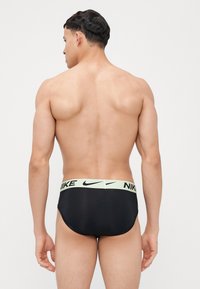 Sorte Nike svømmedrakt med en mintgrønn midjebånd som har merkets logo. Materialet ser glatt og tettsittende ut. Vist fra bak.