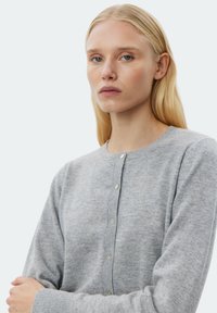 Grå stickad cardigan med rund halsringning, långa ärmar och knäppning framtill med pastellfärgade knappar samt ribbade muddar.