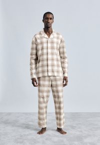 Béžový károvaný pyžamový set vyrobený z jemného materiálu. Košeľa má golier a gombíky; nohavice sú voľného strihu s rovnakým vzorom.