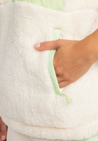 White fluffy fleece pullover with a soft green lining and matching pocket trim. Features a smooth texture and a discreet zipper pull.