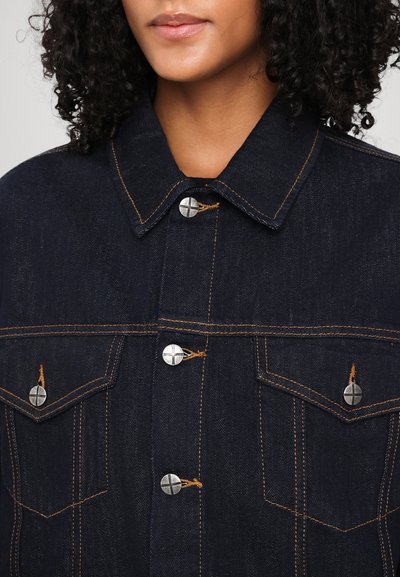 Donkerdenimjack met een klassieke kraag, zilveren knopen, oranje stiksel en twee vo pockets. De stof heeft een gestructureerde afwerking.