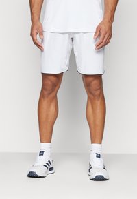 Pantaloni sportivi bianchi con bordi neri, abbinati a scarpe sportive bianche e blu navy. Modello mostrato in piedi, braccia rilassate lungo i fianchi.