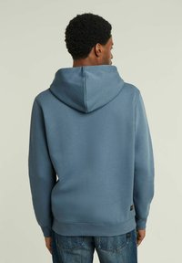 Felpa con cappuccio in morbido tessuto azzurro chiaro uniforme. Presenta una vestibilità ampia e polsini a coste. Dettagli di cucitura sulle spalle e sull'orlo posteriore.