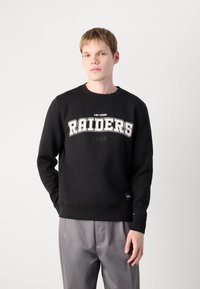 Sweatshirt preto em algodão, com gráfico curvo branco "RAIDERS" e texto "LAS VEGAS". Textura suave, gola redonda e punhos canelados.