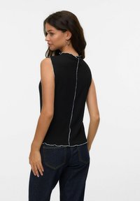 Top nero senza maniche con una texture a costine, caratterizzato da un orlo ondulato e cuciture blu a contrasto lungo la cucitura posteriore. Abbinalo a denim scuro.