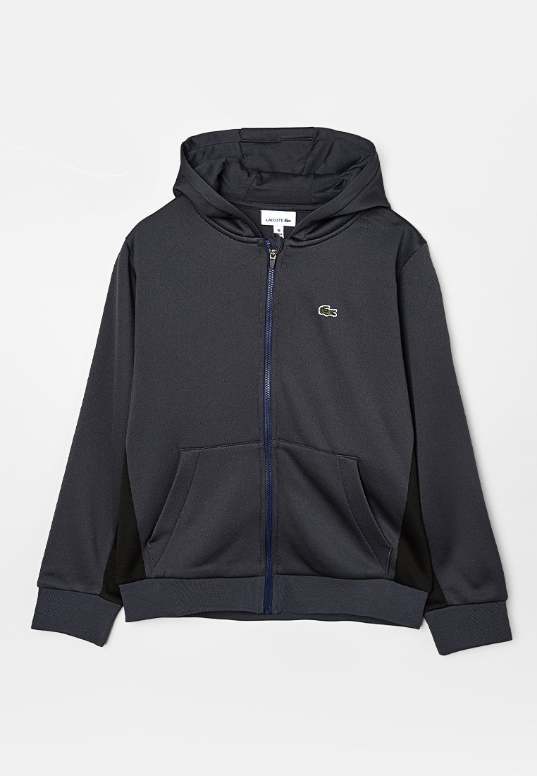 Ciemnoszara bluza z kapturem na zamek błyskawiczny z przednią kieszenią. Posiada sznurek do regulacji kaptura oraz małe zielone logo. Gładki, teksturowany materiał, luźny krój.