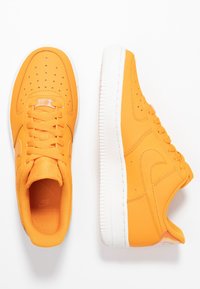 Une paire de baskets orange vif avec des semelles blanches, présent ée en vues de dessus et de côté, avec des lacets et des embouts perforés.