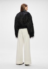 Casaco curto em pelúcia preta com mangas longas, combinado com calças brancas de perna larga e de corte solto. Tecido texturizado com punhos canelados.