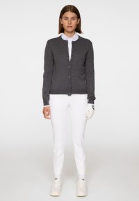 Grå cardigan med rund hals och knappstängning, bärs över en vit skjorta med krage, ihop med vita byxor och handskar. Slät textur.