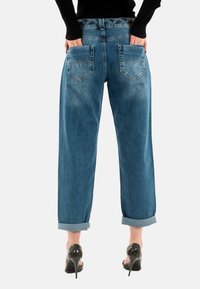 Jeans in denim blu con vita alta, vestibilità ampia, orli arrotolati e due tasche posteriori, che mostrano una texture leggermente sbiadita.