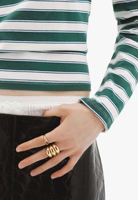 Top de manga larga a rayas verdes y blancas con un dobladillo corto; anillos de oro en los dedos; falda negra texturizada brillante.