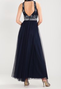Granatowa suknia z tylnym wykończeniem, ozdobiona haftami i dopasowaną górą. Lekki tiulowy dół oraz srebrne szpilki dopełniają całość.