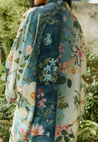Close-up of a person wearing a floral kimono, featuring vibrant blue and cream fabrics adorned with colorful flowers and greenery.