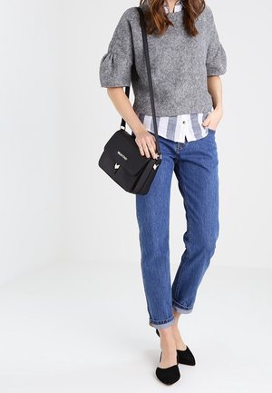 Woman wearing grey puff-sleeve sweater over striped shirt, blue jeans, black pointed flats, and carrying a black shoulder bag.