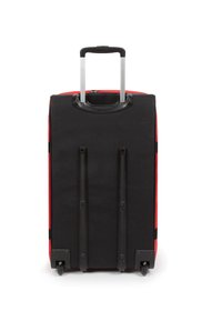 Valise noire avec des accents rouges, surface lisse, poignée rétractable et quatre roues à la base pour la mobilité. Forme carrée avec une texture subtile.