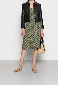 Svart läderjacka, blommönstrad grön klänning, beige sandaler och en halmhandväska. Slim fit, knälång klänning, texturerade material.