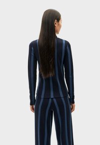Navyblauwe verticaal gestreepte longsleeve top met een aansluitend ontwerp en zachte textuur, gecombineerd met bijpassende broek, gezien vanuit de rug.