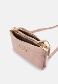 Pink leather crossbody bag with textured surface, two zippered compartments, gold hardware, and an embossed logo detail on the front.