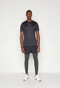 Fekete sportos póló rövid ujjal; fekete rövidnadrág; szürke sportos leggings; fehér cipők barna díszítéssel. Egyszerű, letisztult dizájn.