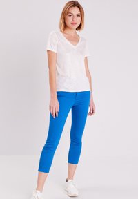 Weißes kurzärmliges V-Ausschnitt-T-Shirt mit strukturierter Oberfläche, kombiniert mit leuchtend blauen, enganliegenden Capri-Leggings und weißen Sneakern.