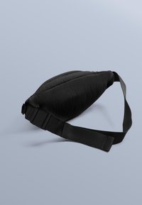 Svart vadderad midjeväska med en mjuk textur och en böjd form. Har en robust svart rem med ett plastspänne för justering.