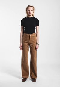 T-shirt noir à manches courtes associé à un pantalon marron taille haute à jambes larges. Le pantalon présente une fermeture à boutons et un tissu texturé.