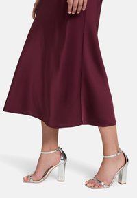 Bordo Satin-Midi-Kleid kombiniert mit silbernen, hochhackigen Sandalen mit Knöchelriemen und Blockabsatz. Glatte Textur, elegantes Design.