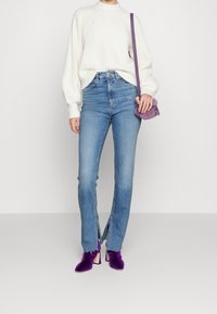 Bílý pletený svetr, světle modré džíny s vysokým pasem a rozparkem na lemech, a fialové sametové kotníkové boty na podpatku. Malá fialová kabelka s popruhem.