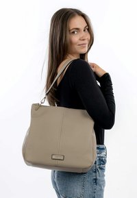 Beige leren tote bag met een gestructureerde vorm, voorzien van een subtiele textuur en een metalen logoaccent aan de voorkant. Verstelbare schouderriem.