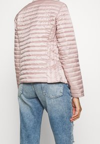 Light pink puffer jacket with quilted design, showcasing a smooth texture and tailored fit, paired with distressed blue denim jeans.