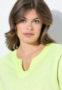 Top giallo neon a maniche corte con una trama sottile e scollatura a V. Il tessuto appare morbido e leggero, adatto per un abbigliamento casual.