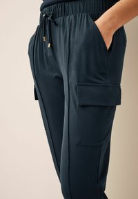 Marineblauwe cargobroek gemaakt van gladde stof met een elastische tailleband, zijzakken en een relaxed fit. Kenmerkt zich door gouden hardware.