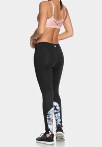 Černé sportovní legíny s akcentem květinového vzoru, přiléhavý střih a elastická látka, kombinované s růžovým sportovním podprsenkou se špagetovými ramínky a černými teniskami.
