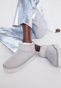 Stivaletti alla caviglia in suede grigio decorati con numerosi strass lucenti, con una suola bianca e una morbida fodera, abbinati a pant metallici argento.