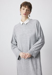 Rochie gri cu mânecă lungă, realizată dintr-un material tricotat moale. Are un guler alb, o croială lejeră, manșete ribiate și o siluetă dreaptă. Design elegant, dar simplu.