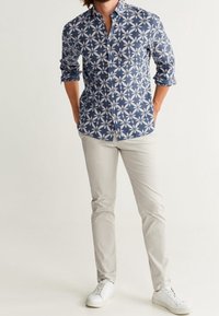 Camicia button-up blu con motivo floreale, abbinata a pantaloni chiari e sneakers bianche. Fit casual e look moderno.