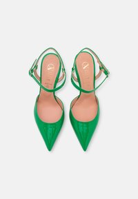 Zielone lakierowane szpilki z wąskimi noskami, paskami na kostkę i gładką fakturą; wkładki posiadają wytłoczone złote logo.