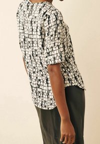 Blusa a maniche corte con motivo in bianco e nero, scollatura rotonda e orlo leggermente curvato. Tessuto liscio con un design strutturato.