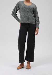 Grauer Strickpullover mit weitem Rundhals, langen Ballonärmeln und strukturiertem Muster, kombiniert mit hochgeschnittenen schwarzen, weiten Jeans und hellbraunen Loafers.