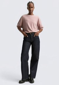 Šviesiai rožinis, didelio dydžio megztinis su trumpomis susuktomis rankovėmis, derinamas su tamsiais plačiomis kojomis džinsais ir juodais tvirtais batais. Paprastas dizainas, be raštų.