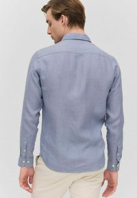 Jasnoniebieska koszula z długim rękawem z mieszanki lnu, posiadająca kołnierzyk, mankiety na guziki oraz prosty tył bez widocznych wzorów czy akcentów.
