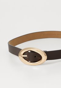 Smeđi kožni pojas s sjajnom zlatnom ovalnom kopčom, s glatkom teksturom i klasičnim dizajnom, ukrašen s "Michael Kors."