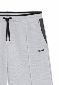 Lichtgrijze jogpants met perforatiepatroon, zwarte trekkoord, zijzak en zwart logo accent. Kenmerkt zich door een contrasterend zwart zijpaneel.