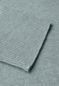 Fondo in tessuto lavorato a maglia grigio chiaro con una texture a coste su una toppa a contrasto. L'area principale è liscia con cuciture sottili.